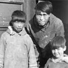 Photograph of an Inuit man and two children standing in a doorway, unknown location, (now Nunavut), unknown date