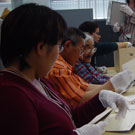 Photograph showing Nunavut residents. Left to right: Sylvia Ivalu, Elders Louis Uttak and Abraham Ulayuruluk, as well as Jesse Mike, at Library and Archives Canada, Ottawa, looking through photographs from the Baffin (Qikiqtaaluk) and Kivalliq (formerly Keewatin) regions, October 2005